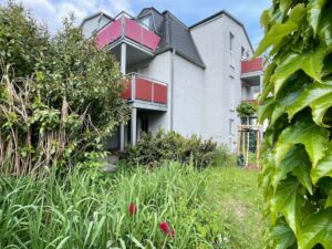 Wohngebäude mit roten Balkonen hinter einer Grünfläche