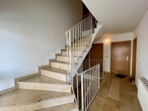 Treppenhaus mit hellen Stufen und weißem Metallgeländer