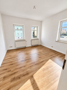 Leerer Wohnbereich mit drei Fenstern und Boden in Holzoptik