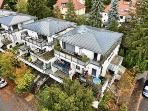 Luftaufnahme eines weißen Mehrfamilienhauses mit Balkonen und Metalldach