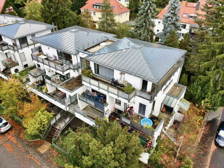 Luftaufnahme eines weißen Mehrfamilienhauses mit Balkonen und Metalldach