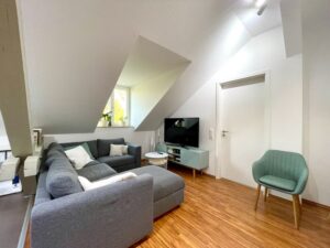 Dachgeschosswohnzimmer mit grauem Ecksofa und Fernseher