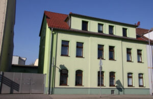 Grünes Mehrfamilienhaus mit rotem Dach – Straßenansicht
