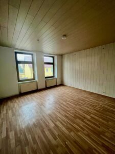 Leeres Zimmer mit Holzdecke, Wandverkleidung und zwei Fenstern