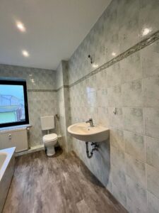 Badezimmer mit grauen Fliesen, Waschbecken, Toilette und Fenster