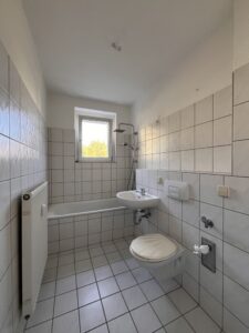 Weiß gefliestes Badezimmer mit Badewanne, Waschbecken, Toilette und Fenster