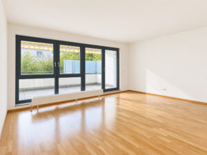 Sonniges leeres Wohnzimmer mit großem Fenster und Balkontür