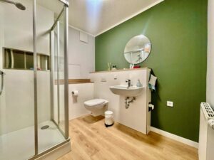Badezimmer mit Dusche, Toilette und grüner Akzentwand