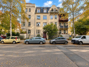 Gelbes Mehrfamilienhaus mit Balkonen an einer baumbestandenen Straße