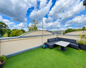Dachterrasse mit Kunstrasen, schwarzem Ecksofa und Tisch