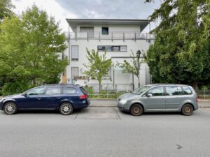 Giebelseite eines weißen Wohnhauses mit geparkten Autos