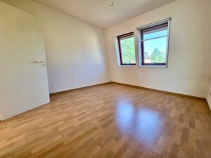 Leeres Schlafzimmer mit zwei Fenstern und Boden in Holzoptik