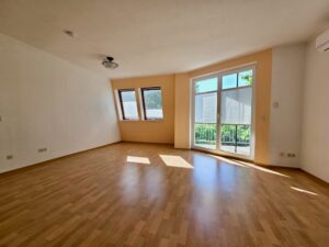 Leeres Wohnzimmer mit bodentiefen Fenstern und Balkonzugang