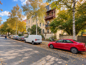 Straßenansicht eines gelben Wohnhauses mit Bäumen und geparkten Autos
