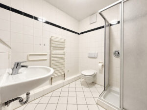 Weiß gefliestes Badezimmer mit Dusche, Waschbecken und Toilette