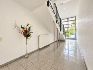 Treppenhaus mit Metallgeländer, grauem Boden und Vase