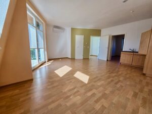 Großer leerer Wohnraum mit Fenstern und offenem Küchenbereich