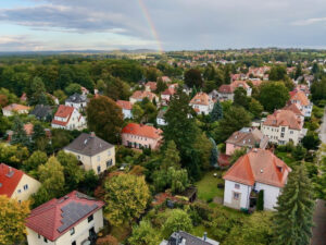 Luftaufnahme eines begrünten Wohngebiets mit Regenbogen
